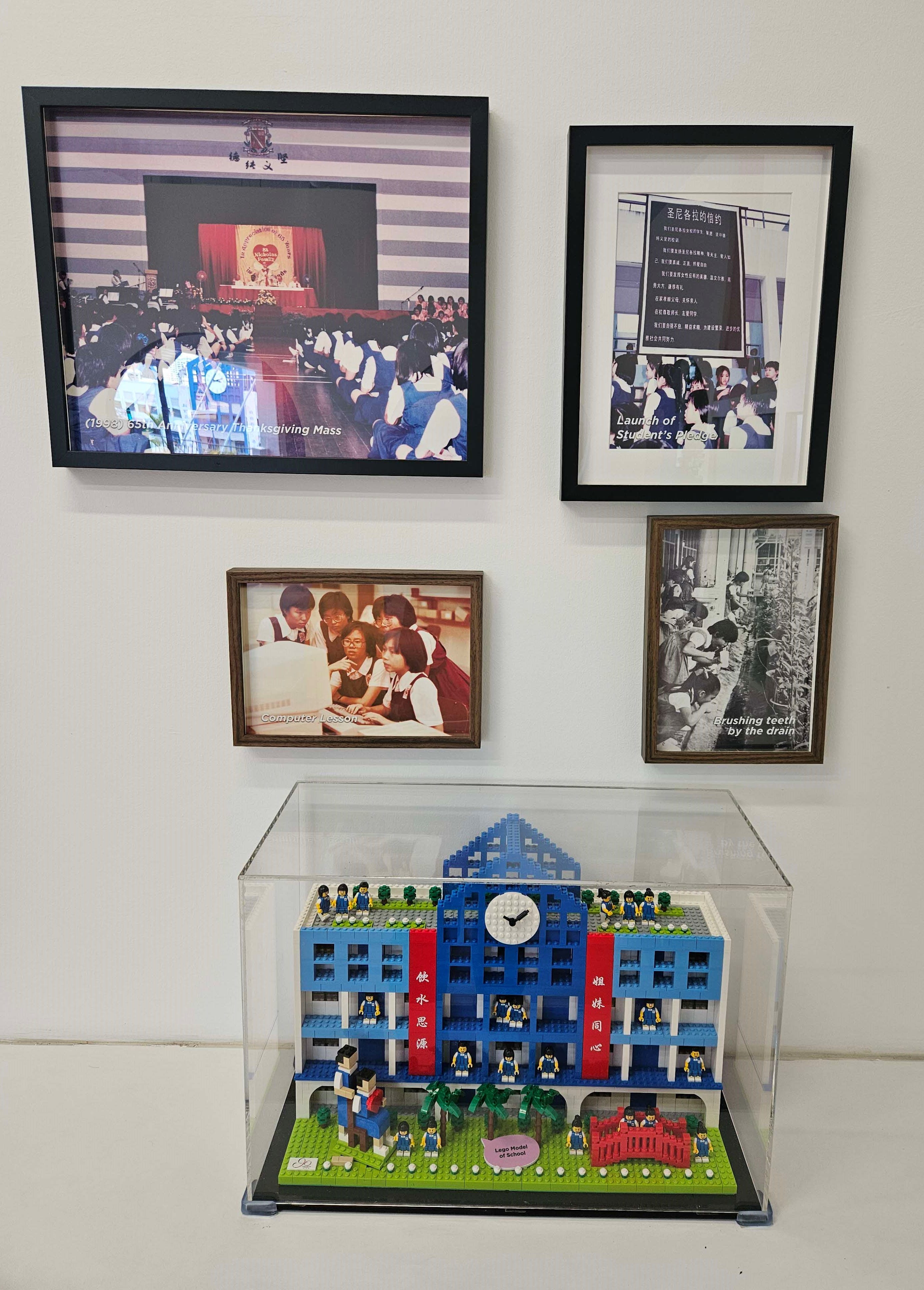 A heritage display featuring four framed vintage photographs on a white wall, captioned '(1958) 65th Anniversary Thanksgiving Mass', 'Launch of Student's Pledge', 'Computer Lesson', and 'Brushing teeth by the drain', depicting scenes from CHIJ St. Nicholas Girls' School's history.
